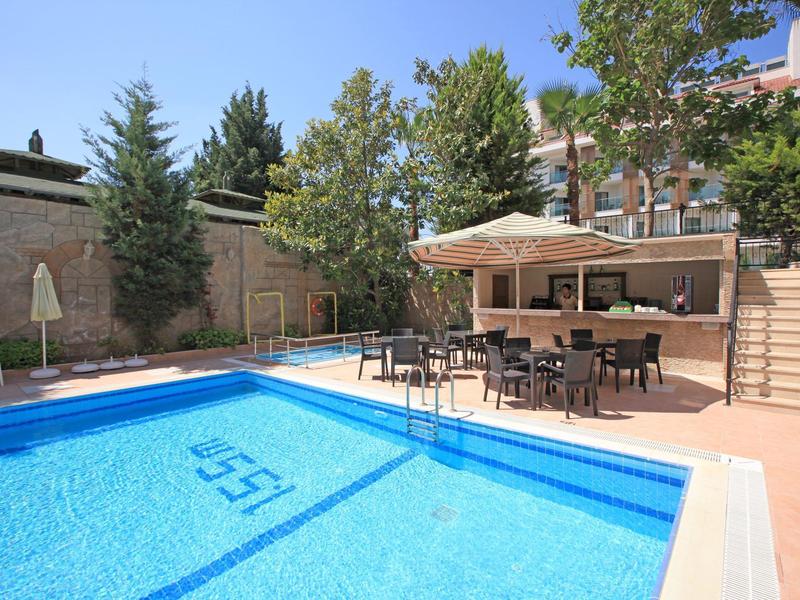 Piscina esterna vuota con tavoli e ombrelloni in un giardino dell'hotel.