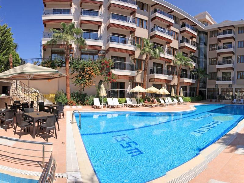 Hotel con grande piscina all'aperto, lettini e ombrelloni sotto un cielo azzurro.