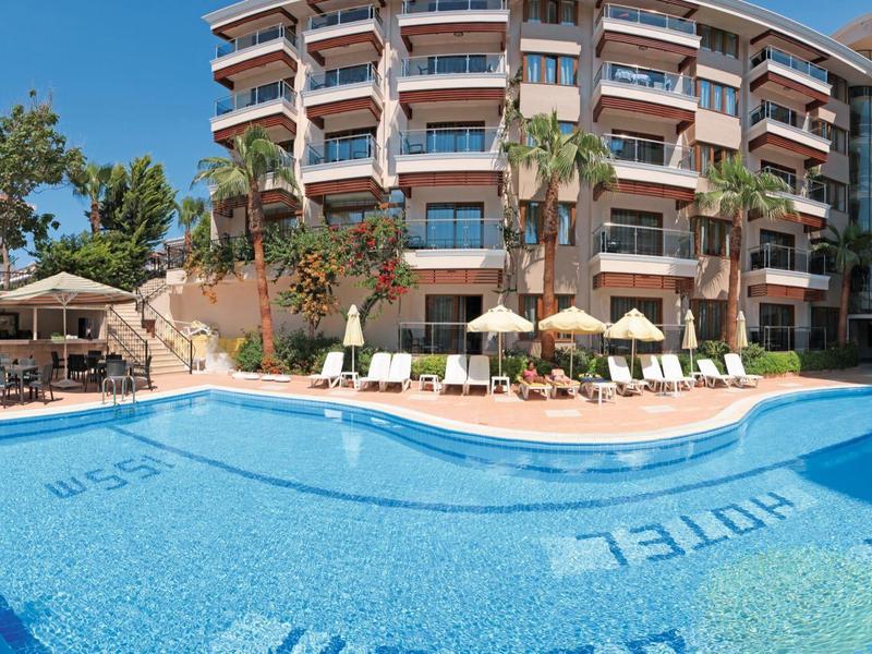 Hotel con piscina all'aperto, lettini e palme sotto un cielo azzurro.