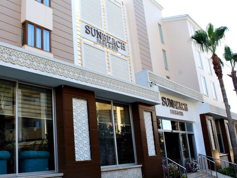 Ingresso moderno dell'hotel con grandi finestre, area salotto e palme davanti.