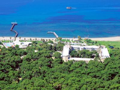 Rotes Strandhotel umgeben von dichtem grünen Wald mit zwei Stegen und blauem Meer im Hintergrund.