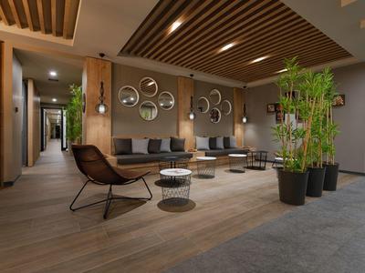 Área de salón moderna en hotel con techo de madera, plantas y muebles elegantes.