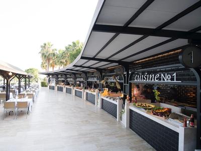 Área exterior moderna de un hotel con puestos cubiertos y asientos, palmeras al fondo.