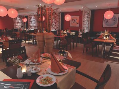 Restaurant mit warmem Licht, runden roten Lampen und gedeckten Tischen mit Servietten und Geschirr.
