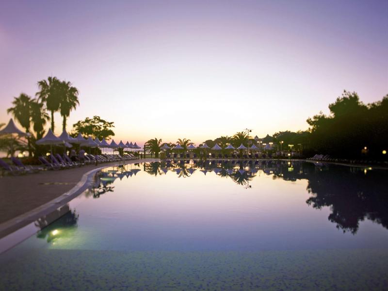 Piscina tranquila con reflejos y palmeras al atardecer en un complejo vacacional.
