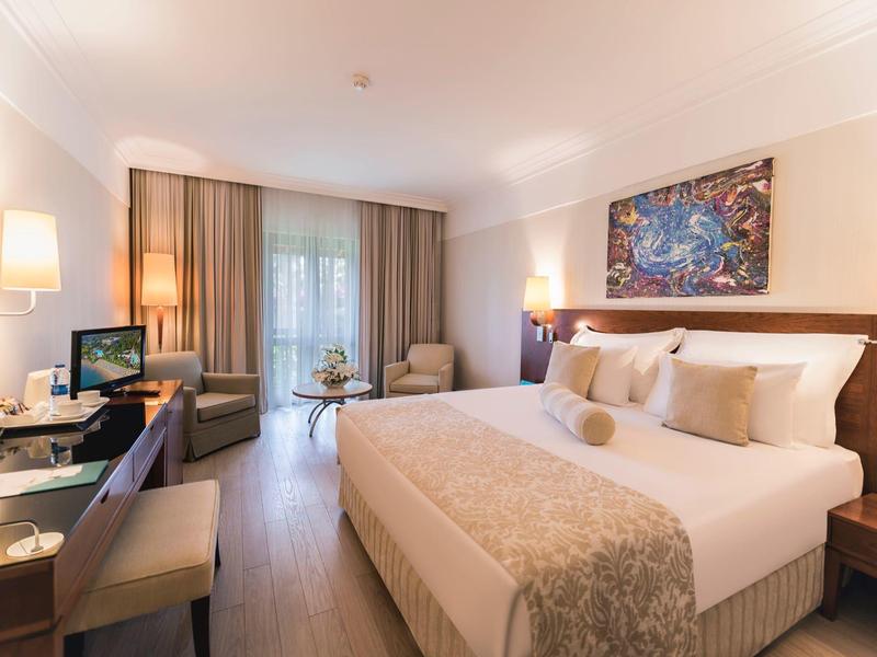 Habitación de hotel luminosa con cama grande, escritorio, sillones y luz de balcón.