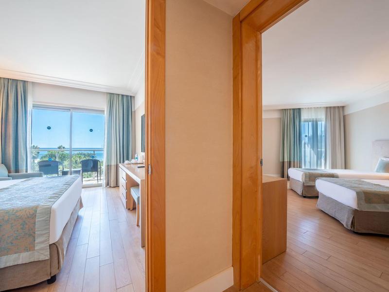 Dos habitaciones de hotel contiguas con muebles de madera clara y grandes ventanas con vistas al exterior.