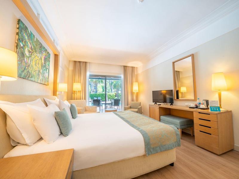 Habitación de hotel luminosa con cama doble, muebles de madera y balcón con vista al verde.