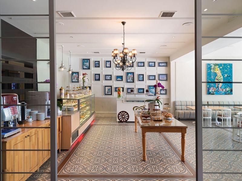 Vista de una cafetería con puertas de vidrio, una mesa de madera y varios cuadros en la pared blanca.