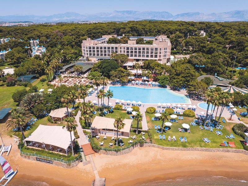Gran hotel con piscina, jardín y acceso directo a la playa, rodeado de árboles y montañas.