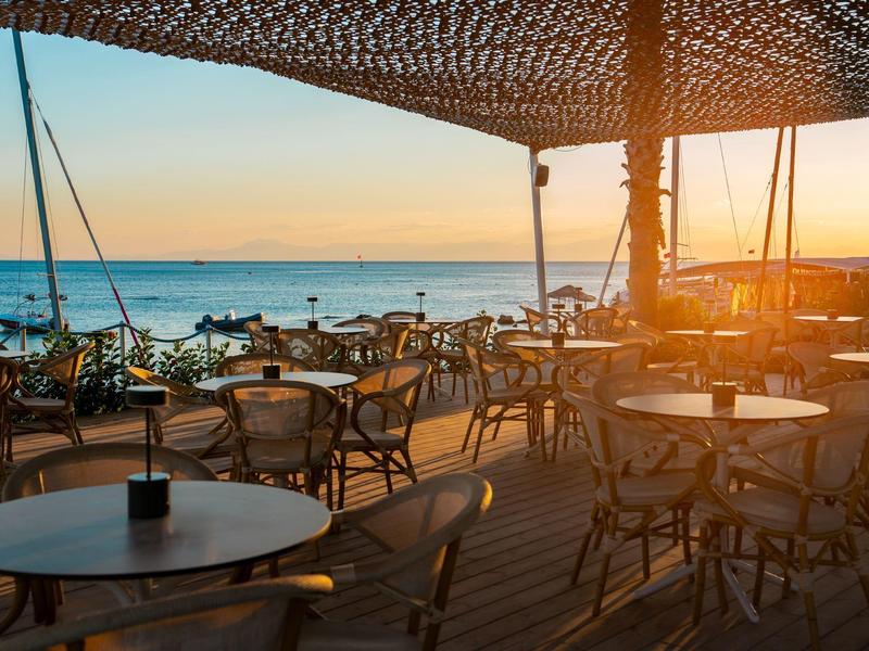 Área vacía de terraza de restaurante en la playa con vista al mar al atardecer.