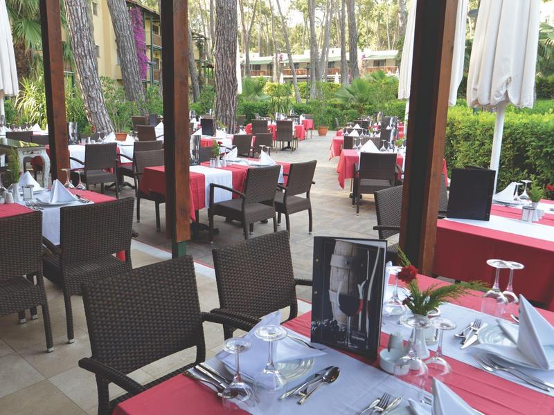 Área elegante al aire libre de un restaurante con mesas vestidas de blanco y manteles rojos.