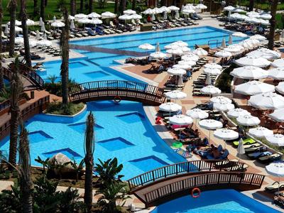 Groot hotelzwembad met meerdere bruggen, ligstoelen en witte parasols onder palmbomen.