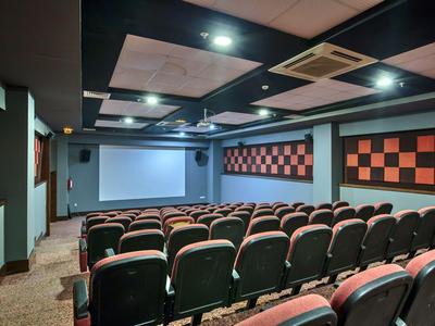 Een kleine bioscoopzaal met rijen rood-zwarte stoelen en een groot scherm aan de voorkant.