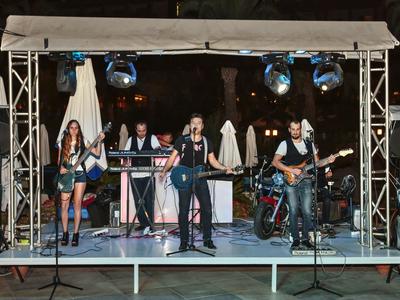 Een liveband met vijf leden die optreedt op een klein podium buiten 's nachts.