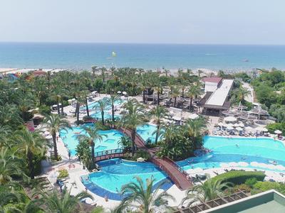 Luchtfoto van een tropisch resort met meerdere zwembaden, bruggen, palmbomen en de zee op de achtergrond.