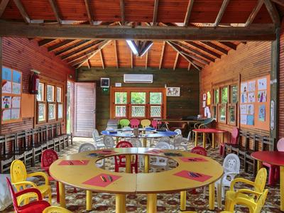 Kleurrijke kinderstoelen en tafels in een gezellige houten klaslokaal met grote ramen.