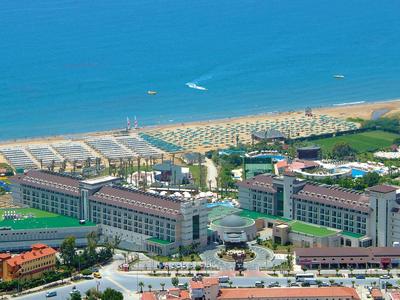Een hotelcomplex aan het strand met meerdere gebouwen, zwembaden en ligbedden bij de zee.