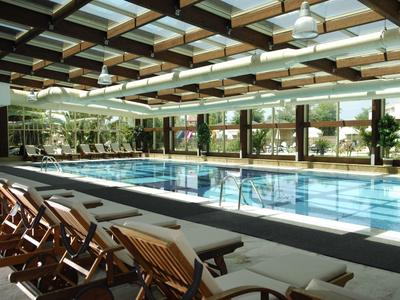 Overdekt zwembad met ligstoelen en grote ramen die buitengroen tonen.