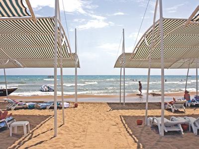 Strandzicht met ligstoelen, parasols en mensen bij de kalme zee onder een deels bewolkte lucht.