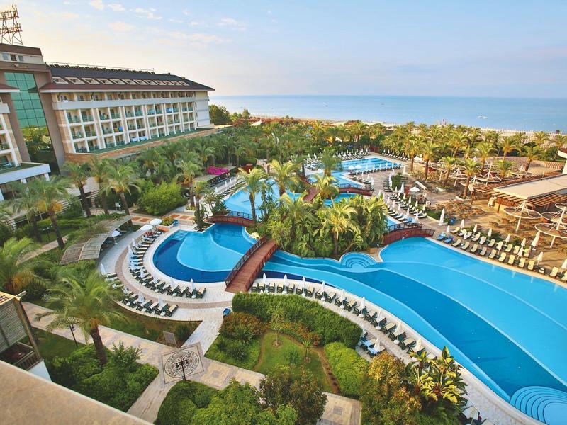 Resort met grote zwembaden, palmbomen, ligbedden en uitzicht op de oceaan onder een blauwe lucht.