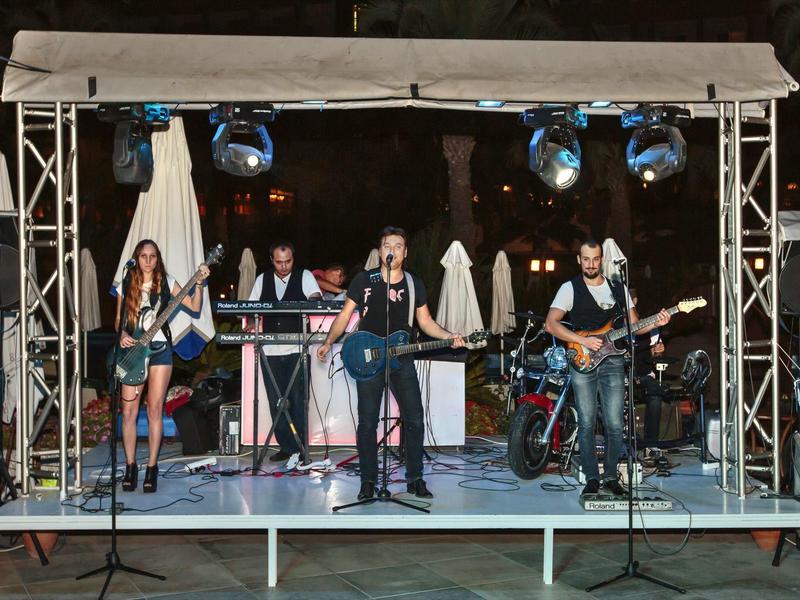 Band treedt 's nachts live op buitenpodium op met instrumenten en blauwe podiumverlichting.