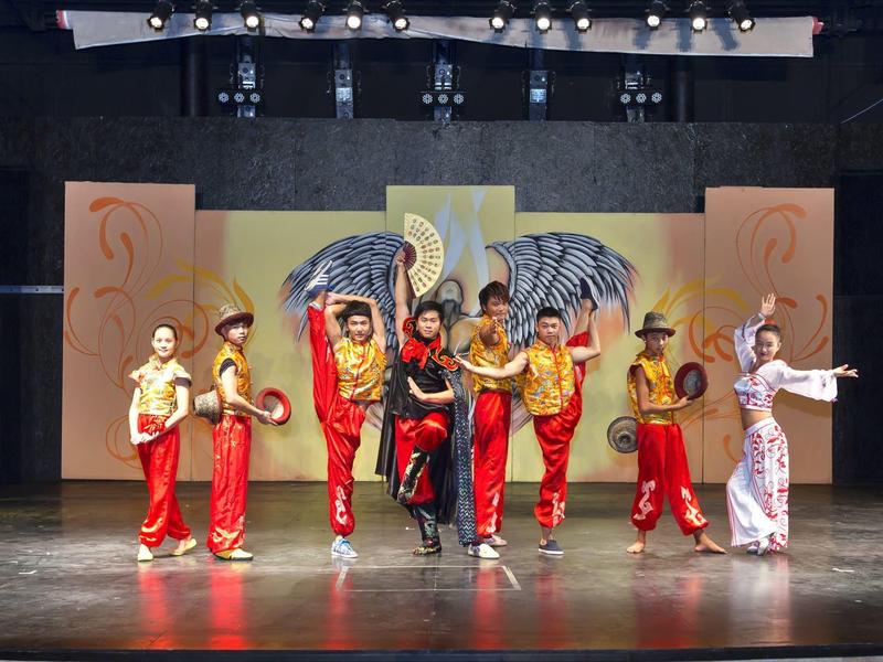 Kinderen in kleurrijke kostuums voeren een dans op het podium uit met een vleugelachtergrond.