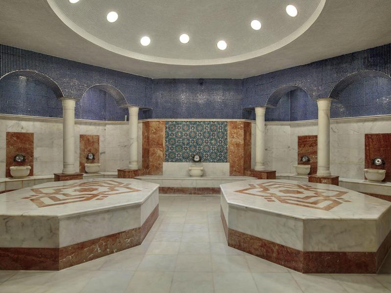 Ruime ronde kamer met marmeren banken en decoratieve muren, voorzien van zachte plafondverlichting.