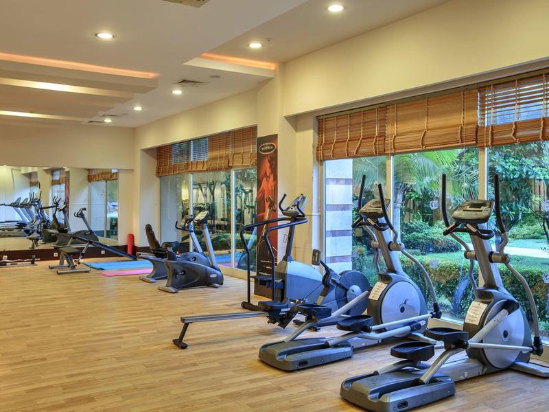 Moderne sportschool met hometrainers, loopbanden en grote ramen met uitzicht op groen.