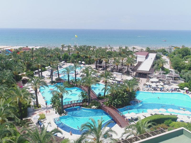 Luchtfoto van een tropisch resort met meerdere zwembaden, bruggen, palmbomen en de zee op de achtergrond.