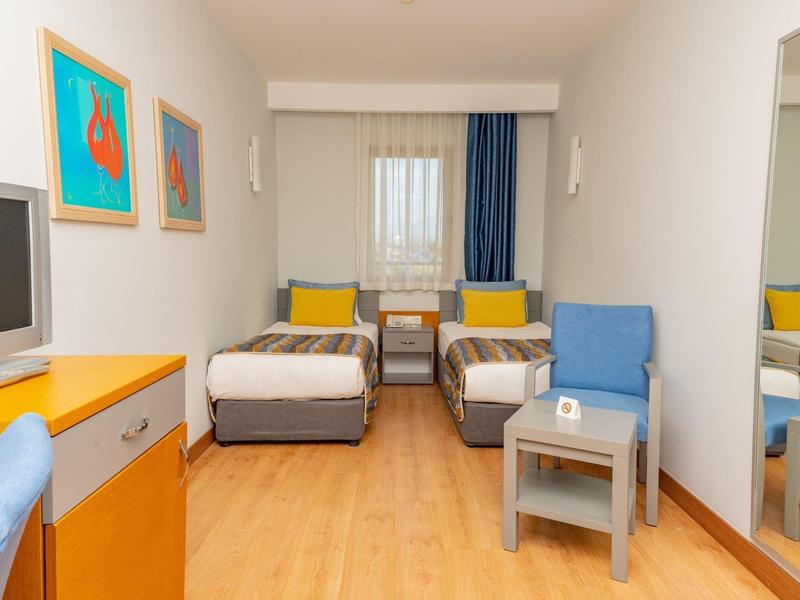 Lichte hotelkamer met twee eenpersoonsbedden, blauwe stoelen en tv.