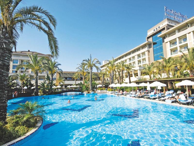 Buiten zwembad van hotel omringd door palmbomen en ligstoelen onder een heldere blauwe lucht.