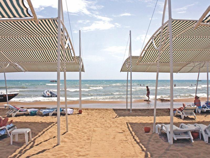 Strandzicht met ligstoelen, parasols en mensen bij de kalme zee onder een deels bewolkte lucht.