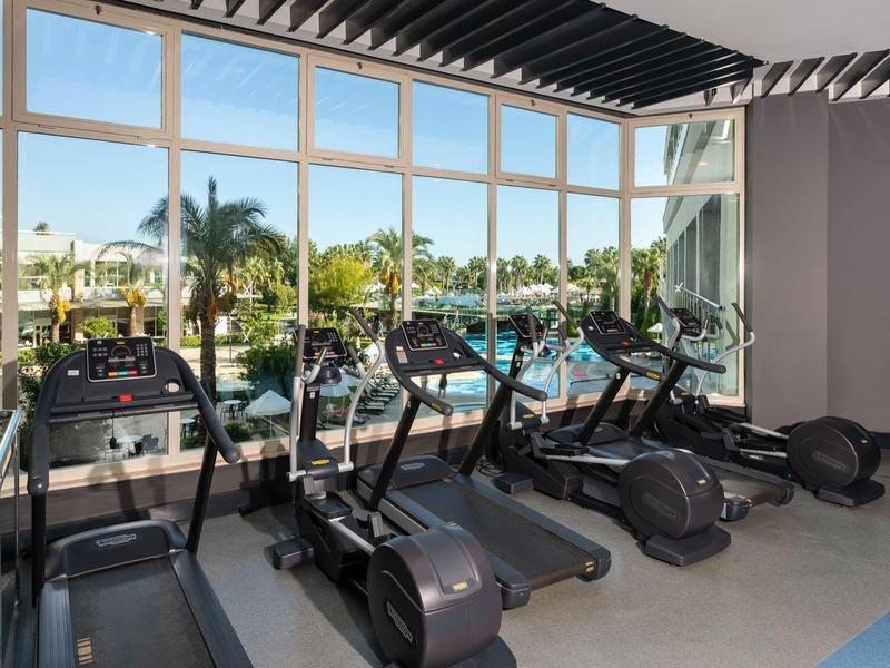Jasna siłownia hotelowa z kilkoma bieżniami przed dużymi oknami.