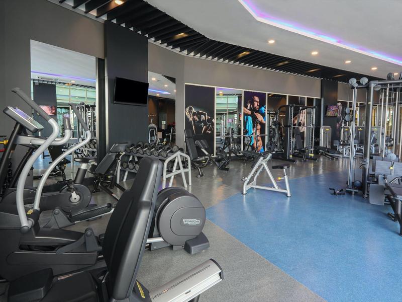 Nowoczesna siłownia z różnorodnym sprzętem i częściowo niebieską podłogą.