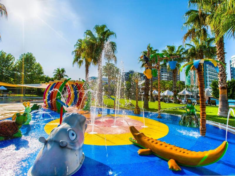 Kolorowy wodny plac zabaw z zwierzętami i fontannami otoczony palmami.