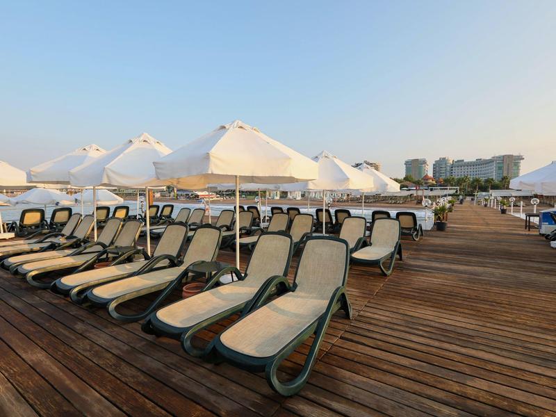 Leżaki z białymi parasolami na drewnianym tarasie przy wodzie.