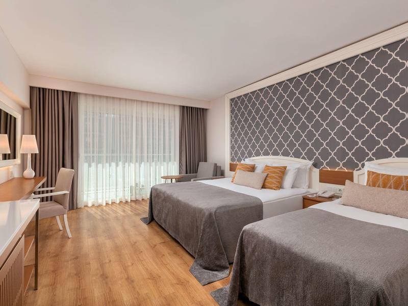 Nowoczesny pokój hotelowy z dwoma podwójnymi łóżkami, dużym oknem i eleganckim wystrojem.