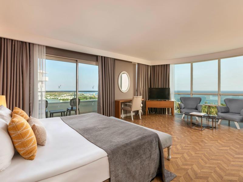 Przestronny pokój hotelowy z łóżkiem podwójnym, fotelami, balkonem i widokiem na morze.