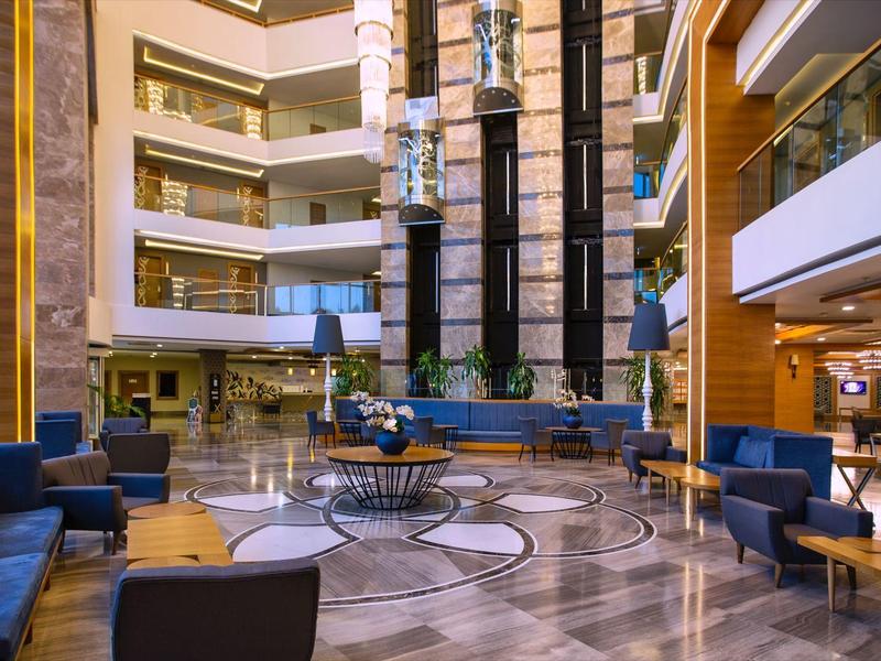 Przestronny hol hotelowy z niebieskimi kanapami i błyszczącą marmurową podłogą.