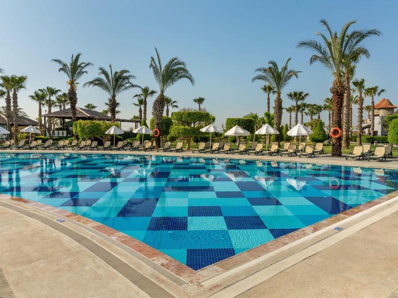 Basen z niebieskimi kafelkami i leżakami pod parasolami przy basenie.