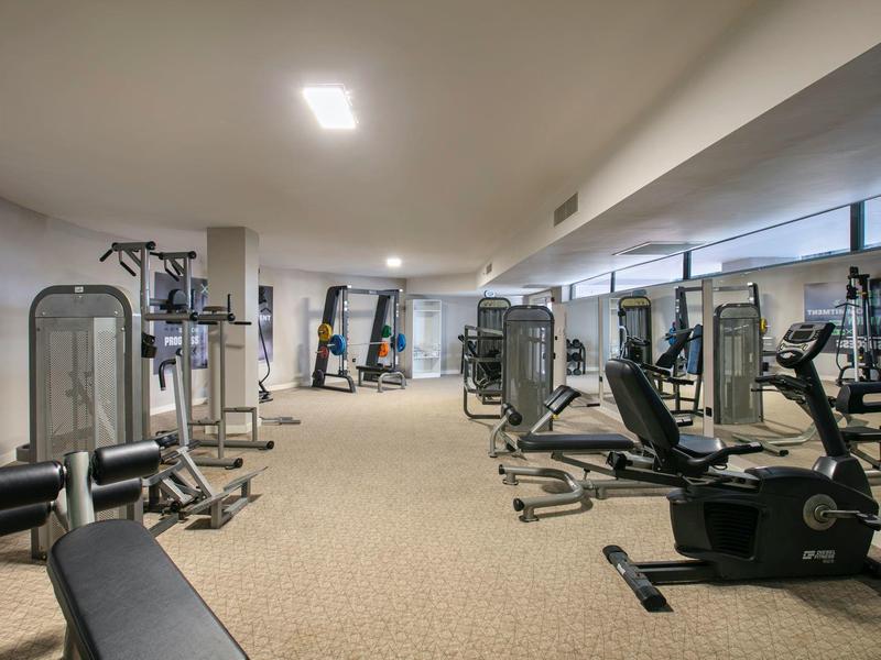 Gimnasio bien iluminado con varios equipos de entrenamiento y pared de espejos.