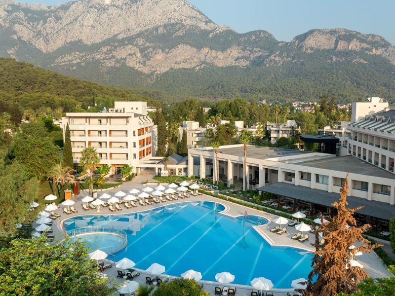 Gran piscina exterior en un hotel vacacional con montañas al fondo y muchas tumbonas.