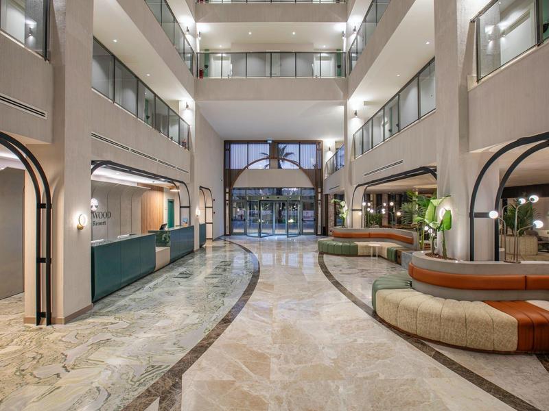 Vestíbulo de hotel luminoso con suelo de mármol, recepción a la izquierda y área de descanso a la derecha.