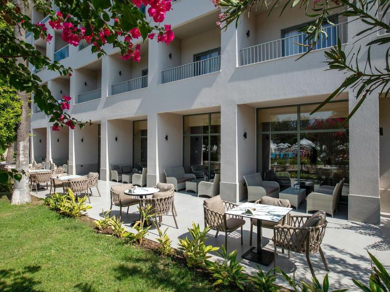 Área exterior de un hotel con mesas, sillas y jardín circundante bajo árboles en flor.