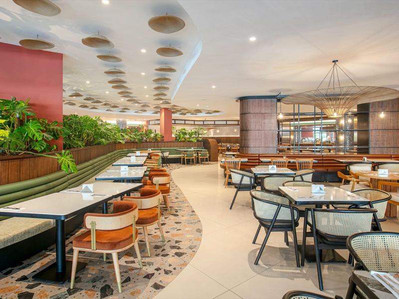Amplio comedor moderno con mesas, sillas y muchas plantas para huéspedes del hotel.