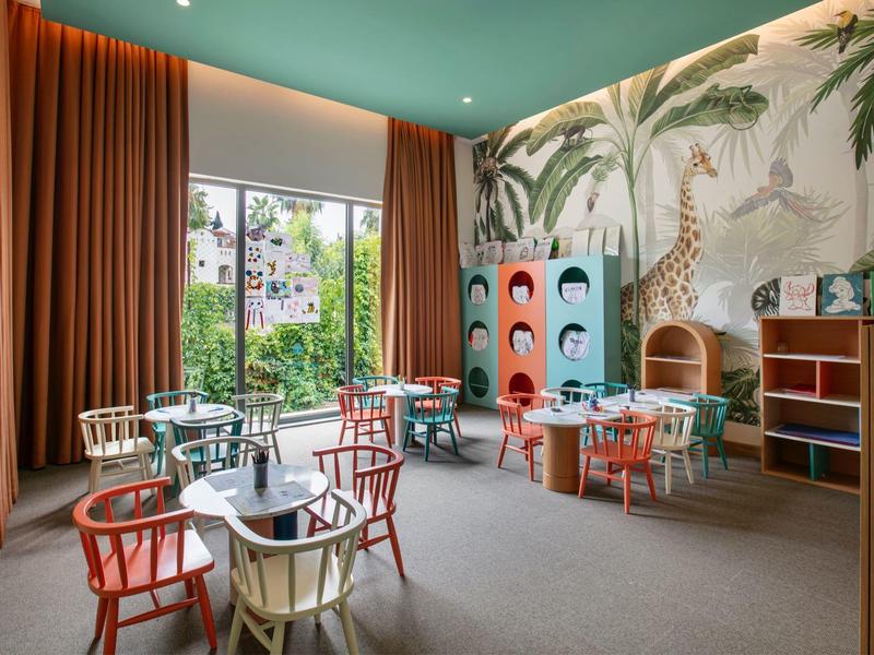 Sala de juegos infantil luminosa con mesas, sillas de colores y decoración temática de safari.