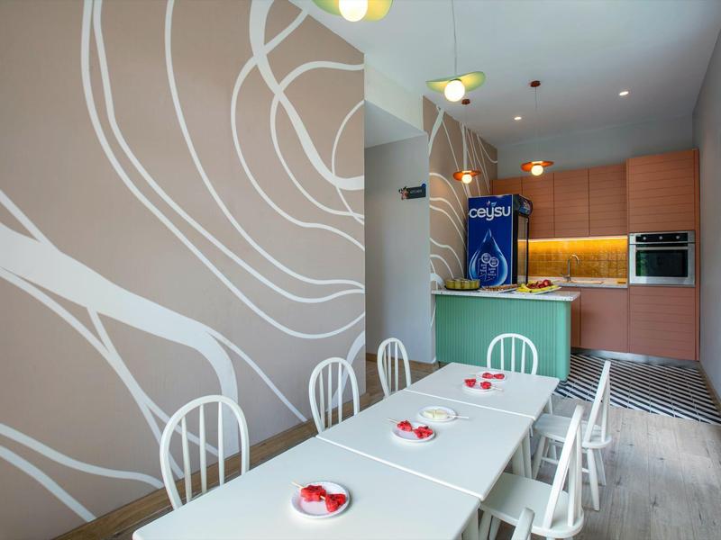 Área de comedor moderna con mesa larga, sillas blancas y decoración mural en una habitación de hotel.