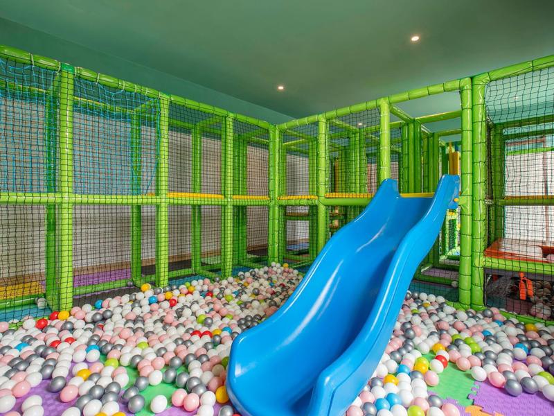 Área de juegos interior colorida con tobogán azul y piscina de bolas en una sala de hotel.