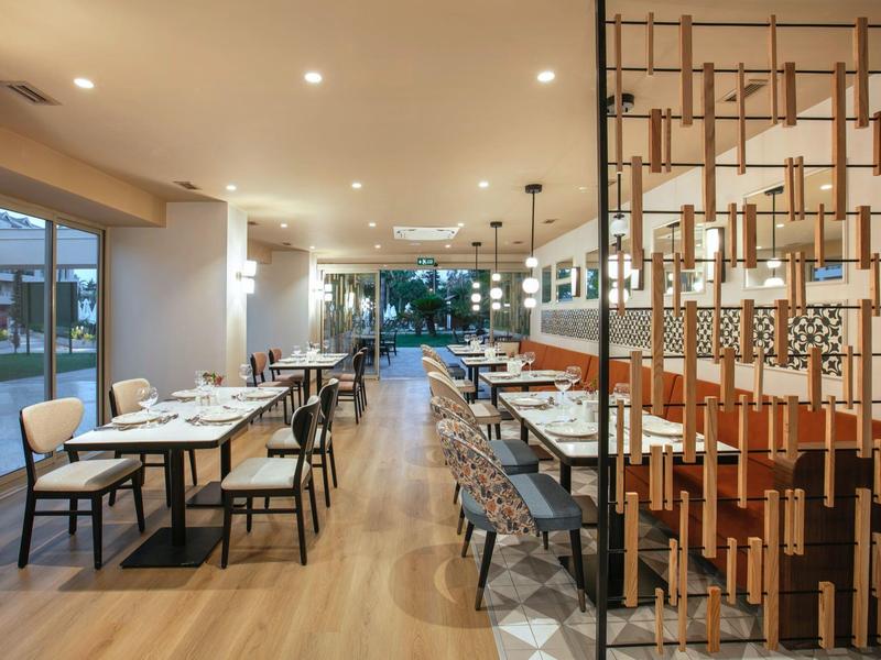 Restaurante moderno con suelo de madera, mesas puestas y luz cálida.